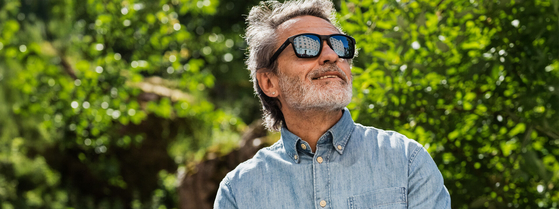 Mies hymyilee auringonpaisteessa, kasvoilla aurinkolasit